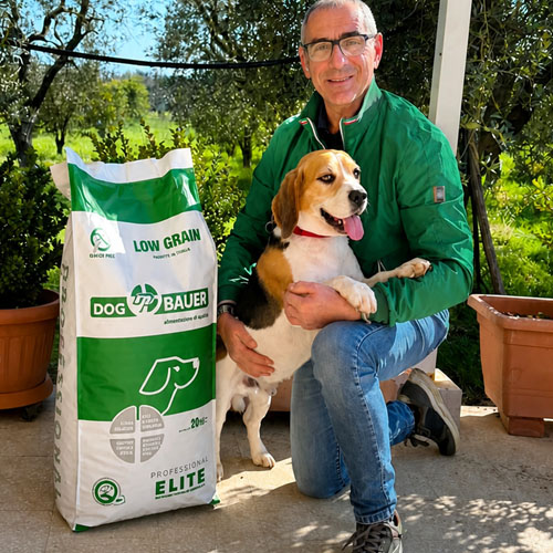 Uomo accovacciato con due cani Boxer e sullo sfondo sacco di crocchette Dogbauer