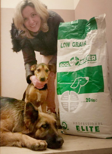 Signora bionda con un cane da Pastore Tedesco, un meticcio e il sacco delle crocchette Low Grain Dogbauer